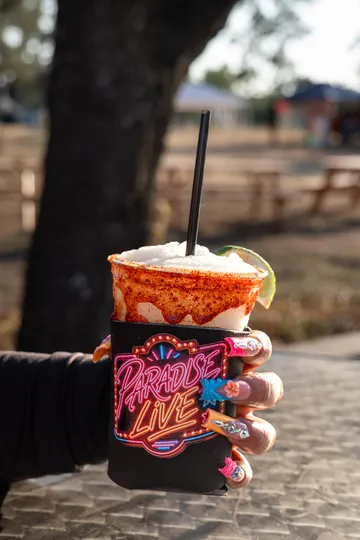 A Paradise Live branded drink koozie held up outdoors at the car show