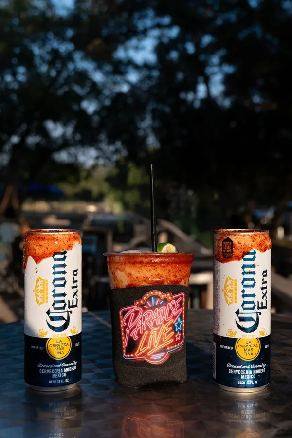 A Paradise Live neon koozie next to chelada-rimmed Coronas