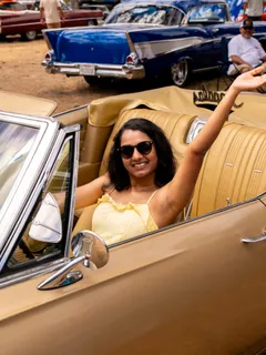 A woman waving from a gold classic convertible at the Paradise Live car show