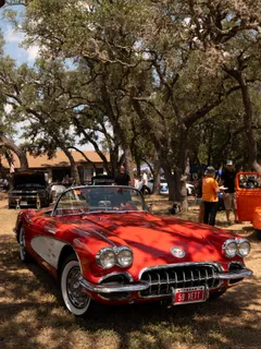A red vintage Corvette convertible parked under the trees at Paradise Live