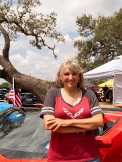 A woman posing beside her Corvette under an American flag at Paradise Live