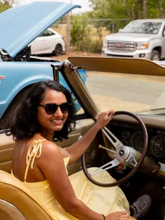 A woman smiling behind the wheel of a gold classic convertible