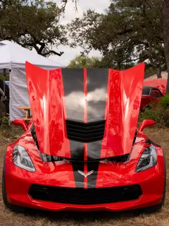 A red Corvette with black racing stripes and its hood raised