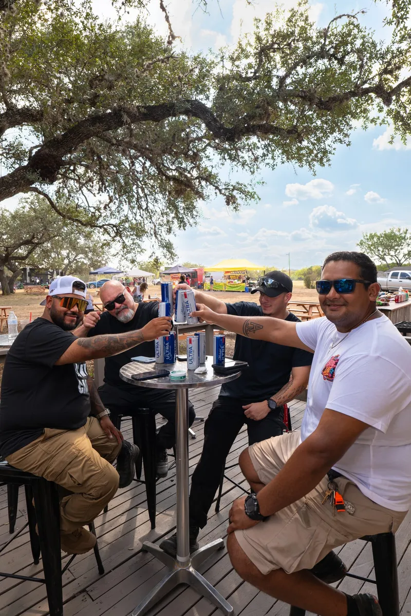 Friends toasting with cans around a table at the Paradise Live car show