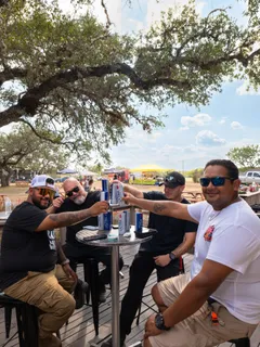 Friends toasting with cans around a table at the Paradise Live car show